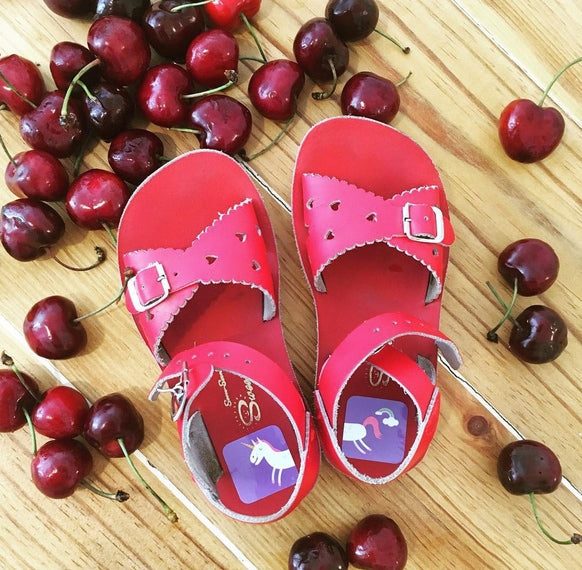 Laufkleber mit Fabelwesen-Motiven wie Einhorn und Drache, in offenen Kindersandalen angebracht. Die bunten Aufkleber helfen Kindern, spielerisch den linken vom rechten Schuh zu unterscheiden, und bleiben auch bei Bewegung und warmem Wetter zuverlässig haften.